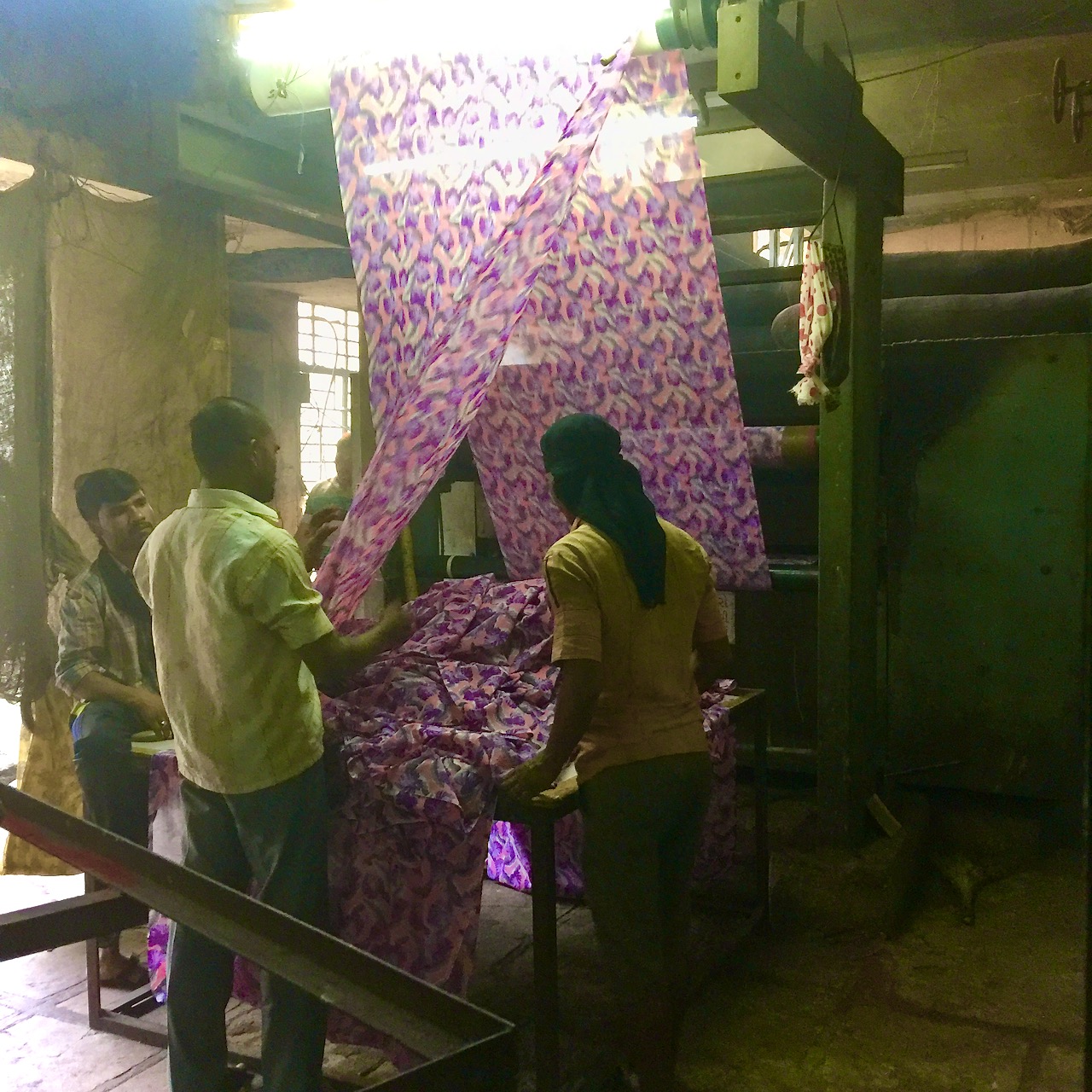 Three worker examine a sheet of fabric in a textile mill