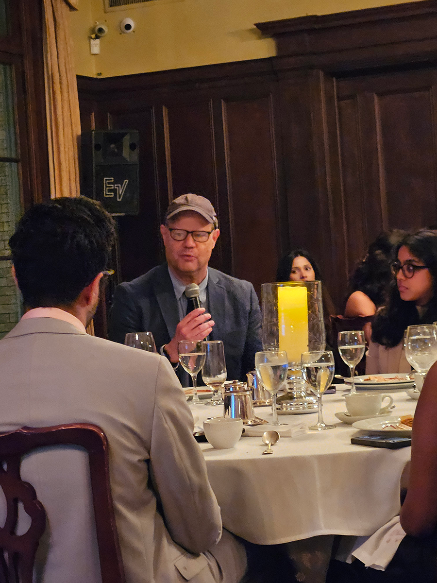 A man in a jacket and baseball hat speaks to students