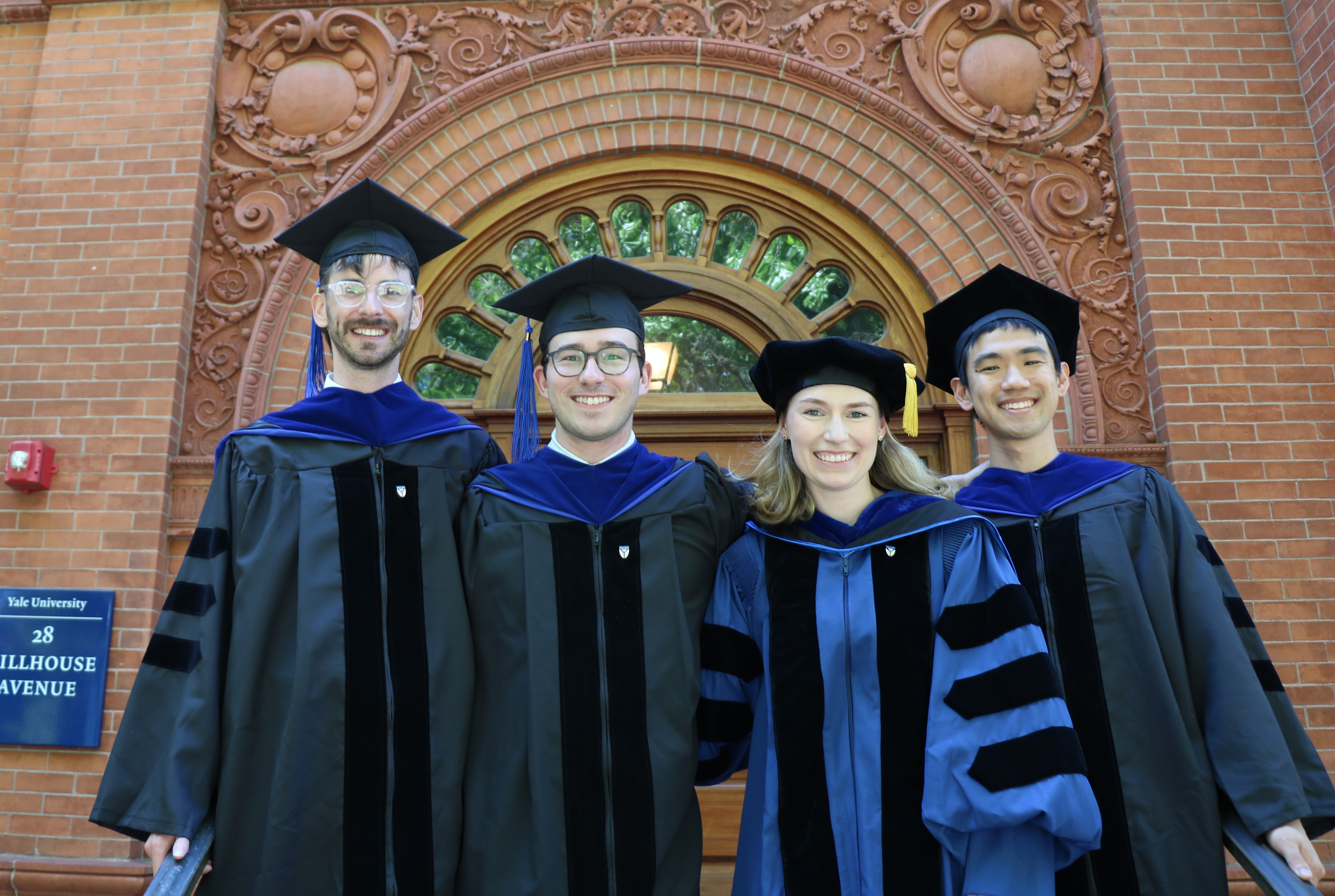 4 graduates on the steps of the Yale Economics Building.