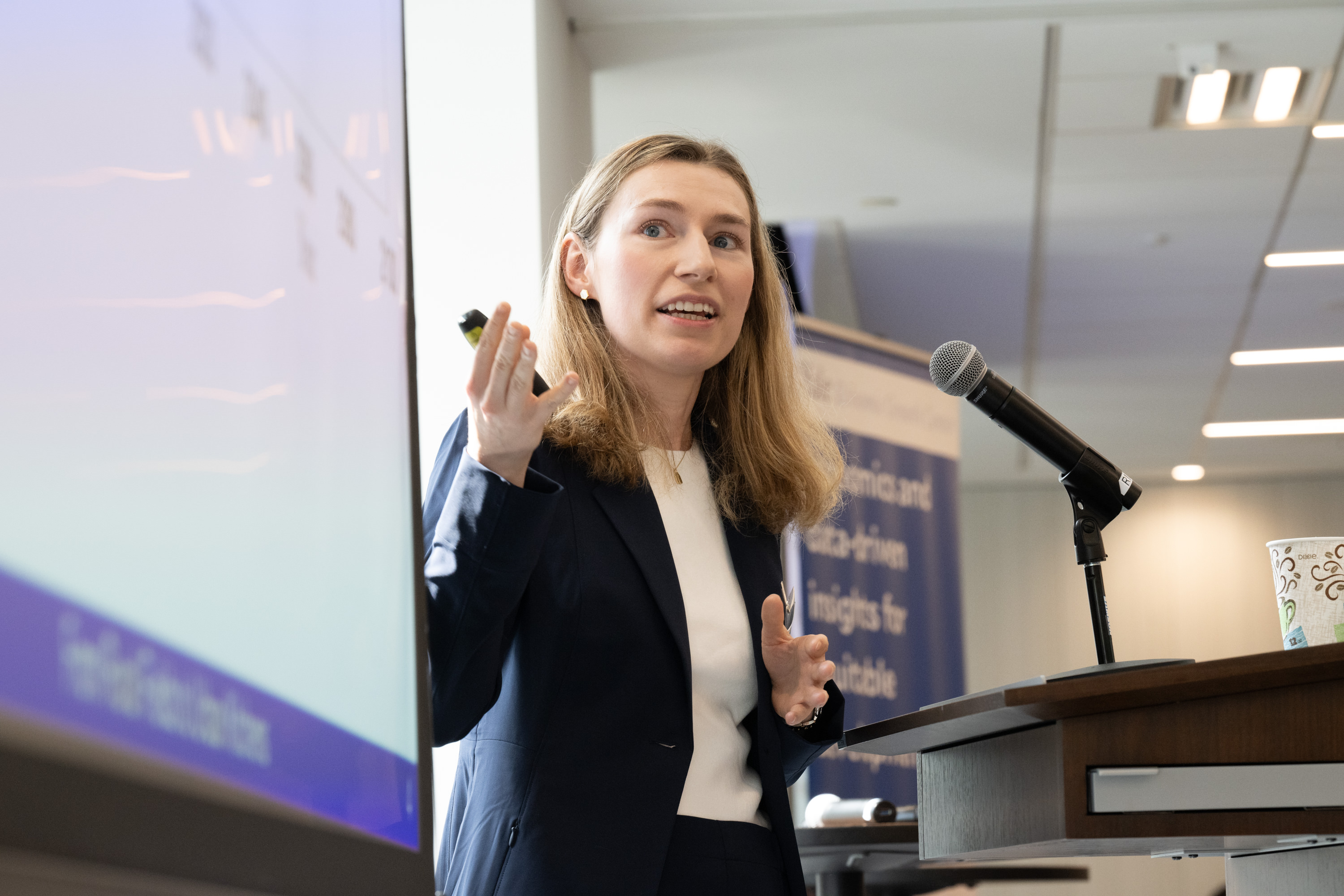 A woman in a dark jacket speaks to an audience
