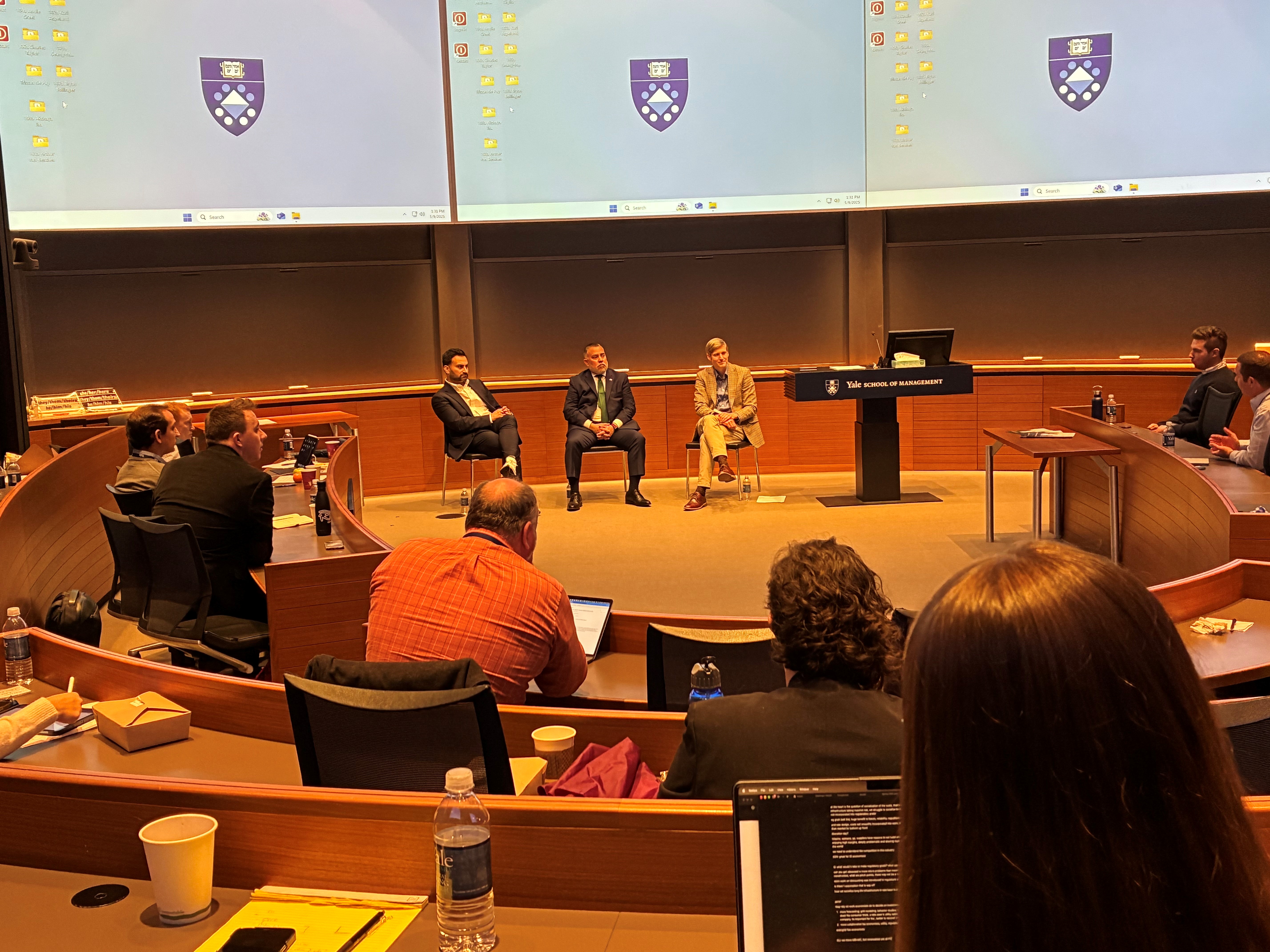 Three men sit at the front of a classroom to answer questions from an audience