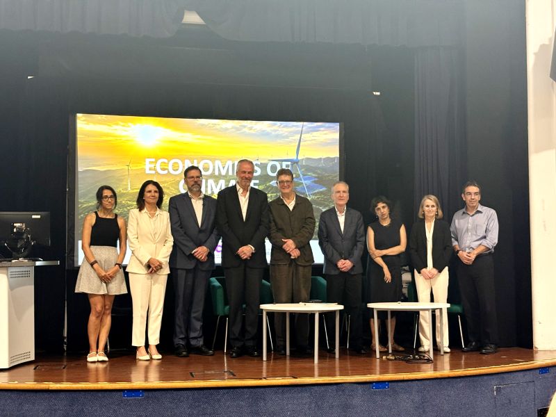 ine speakers pose together on stage following an 'Economics of Climate' panel discussion