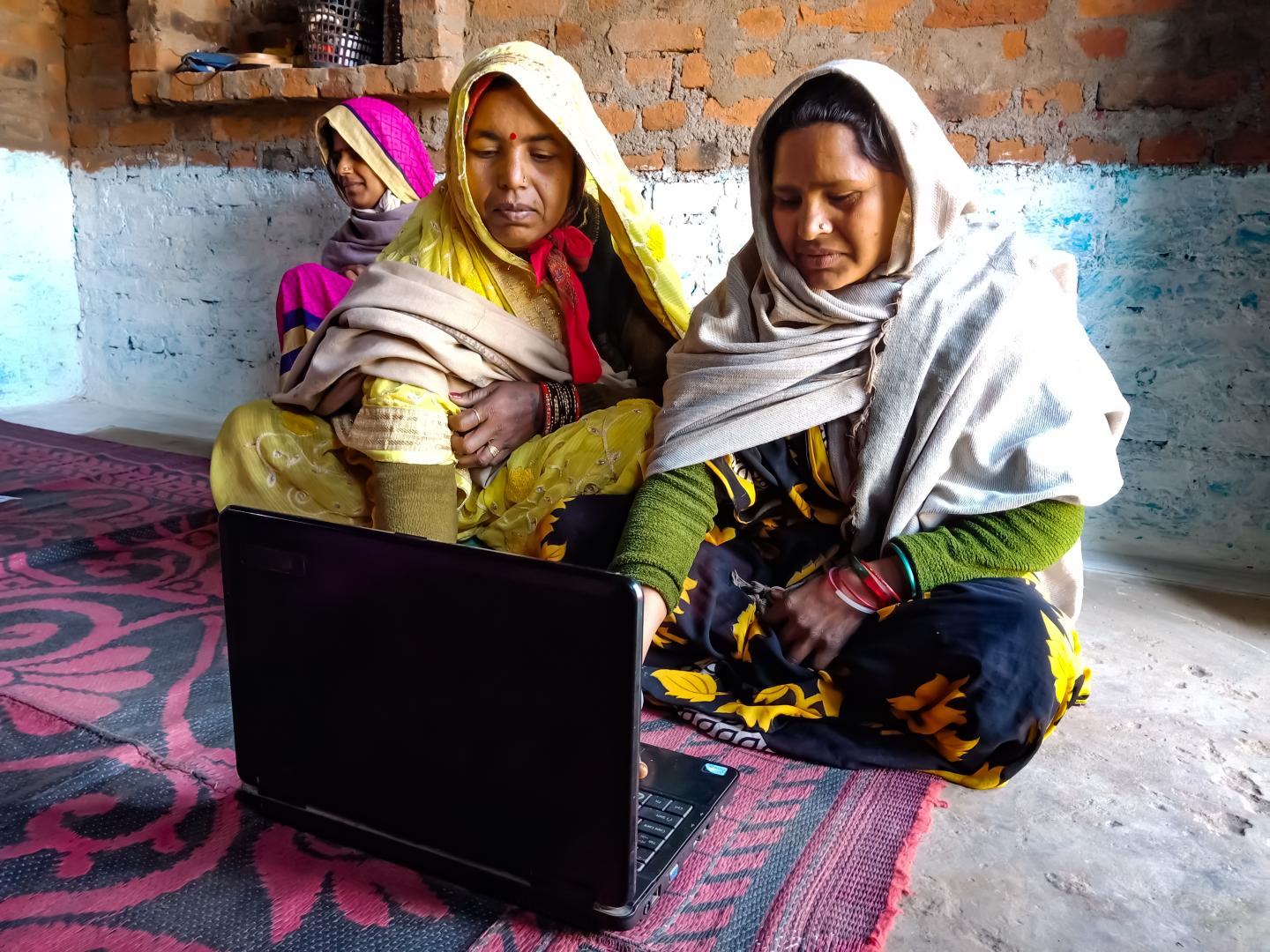 Two Indian women sitting on carpet looking at a computer. 