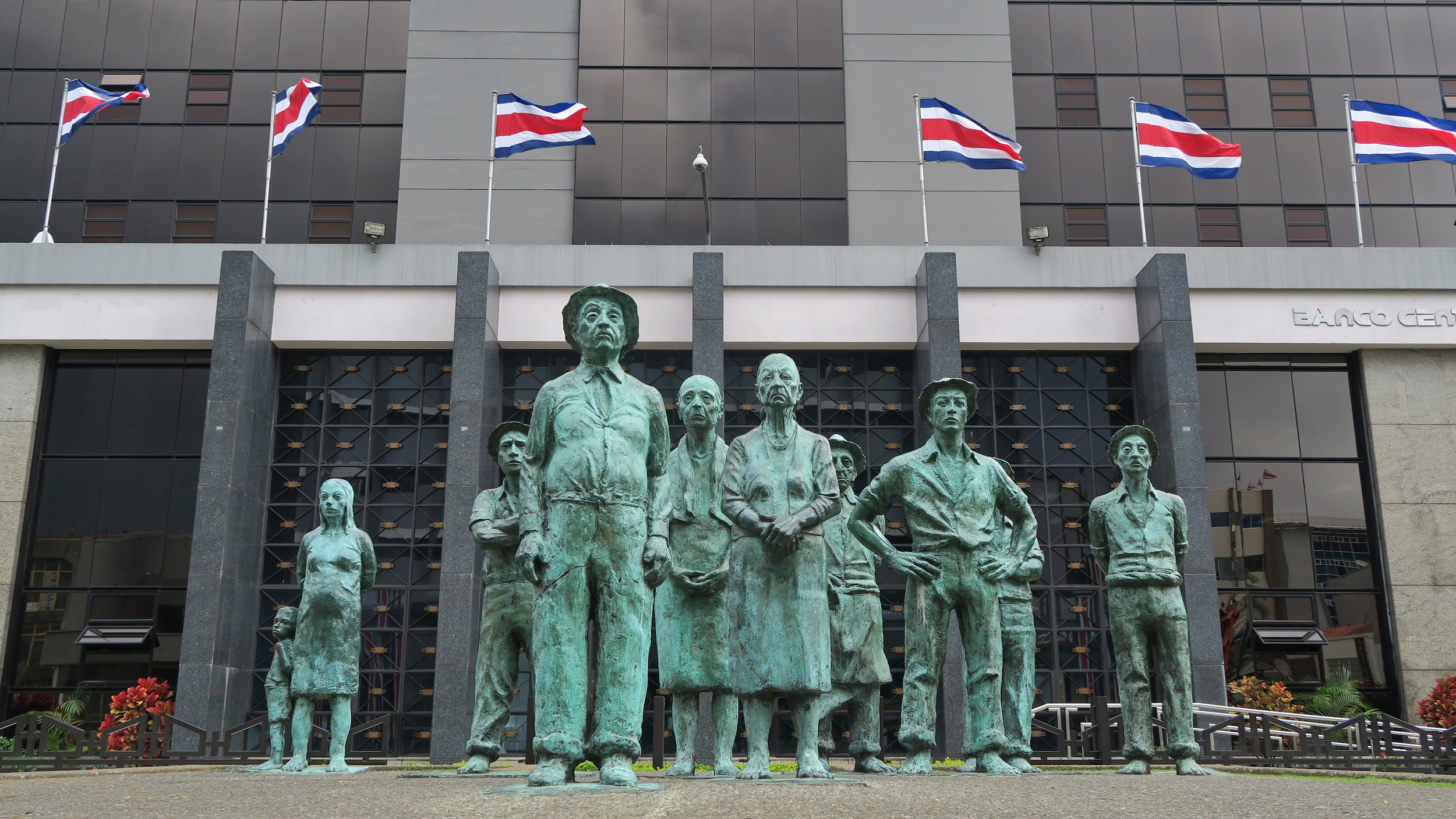 A statue of common people in front of a large, modern building