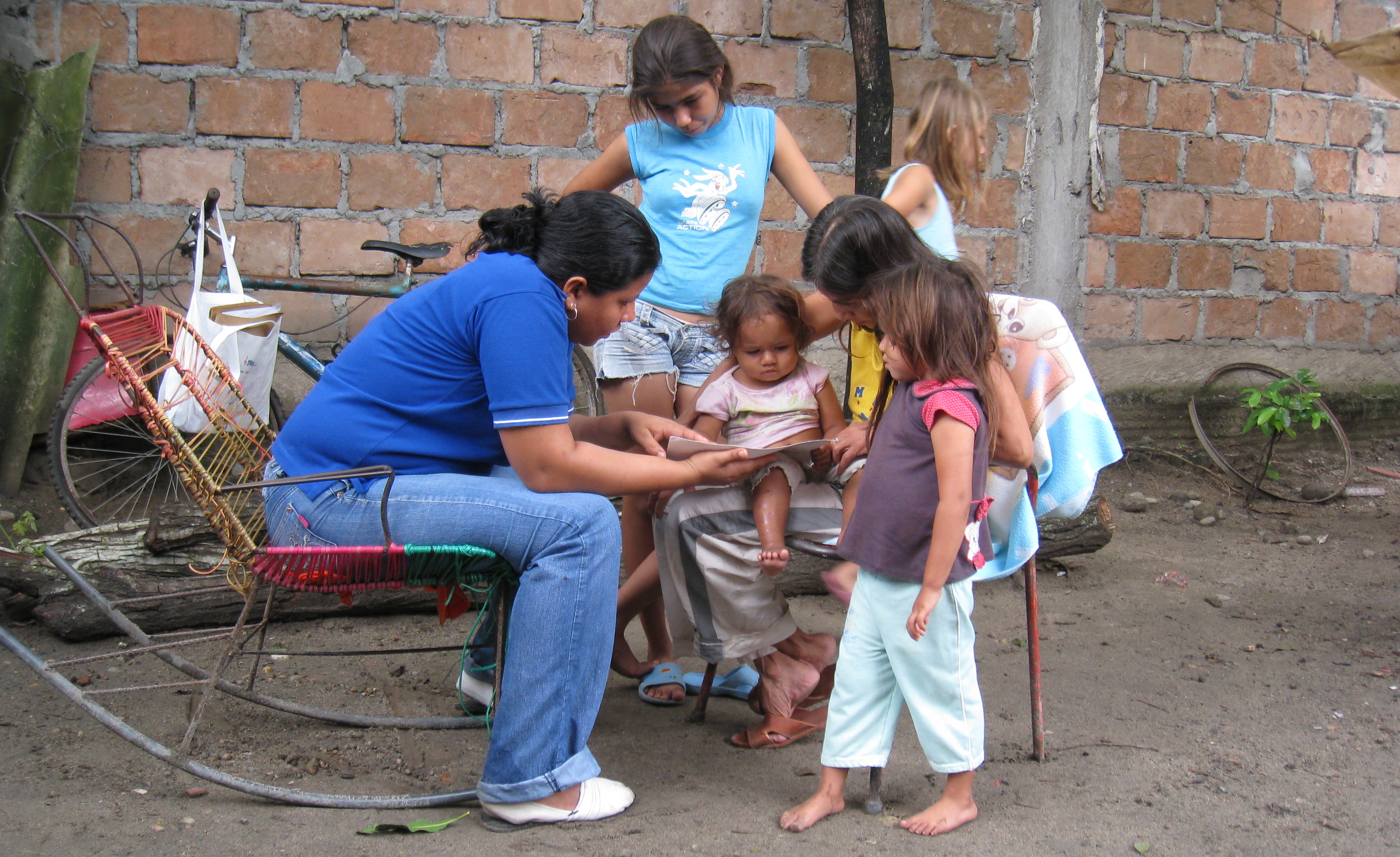 In a dusty courtyard, two women show a young girl a toy.