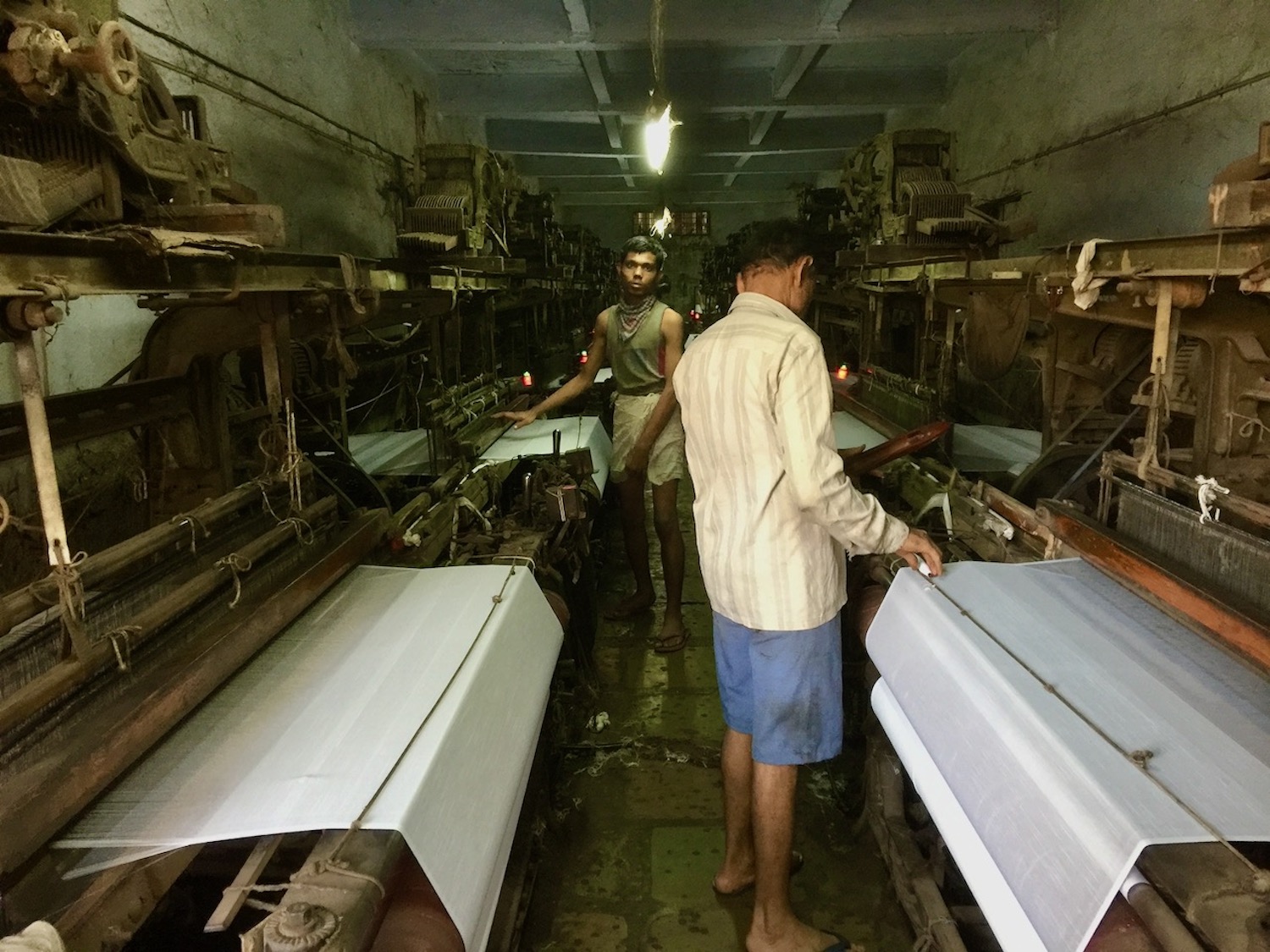 An older man and a younger man, working in a cramped factory.