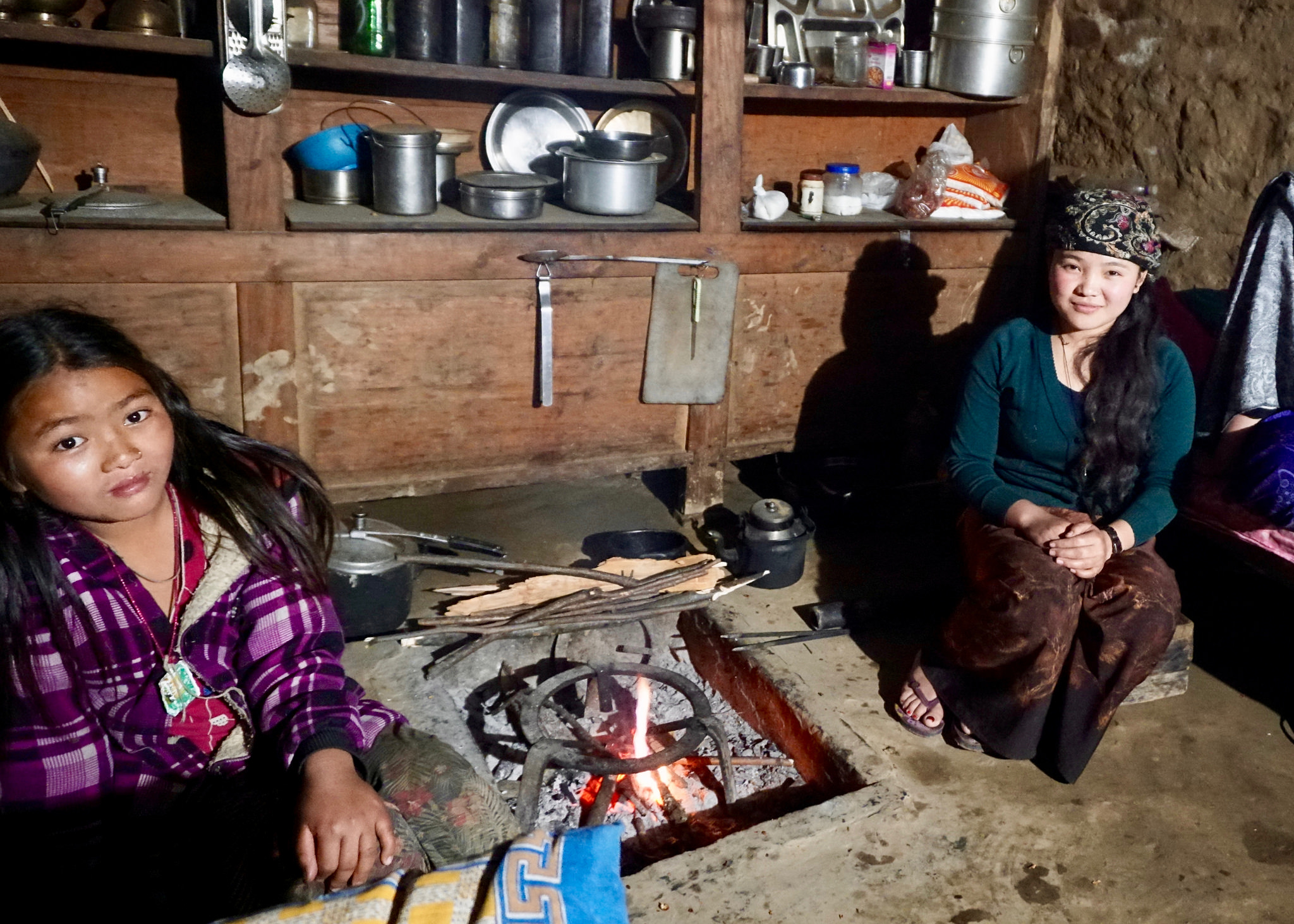 Two women sit next to an indoor cookstove