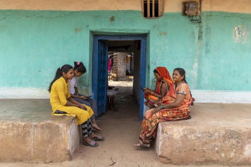 Four women sitting in front of doorway. Two are on mobile phones.