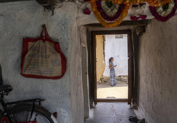An interior view of a white-walled building, looking out at a young woman standing in the doorway.