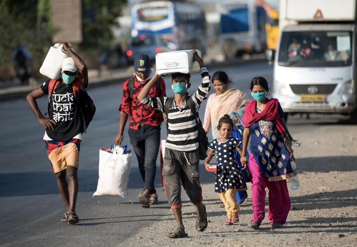 Families in masks walking with grocery items on road.