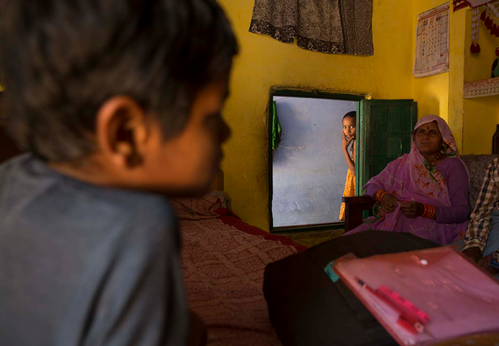 Family sitting a room, with a young girl peering in from the doorway. 