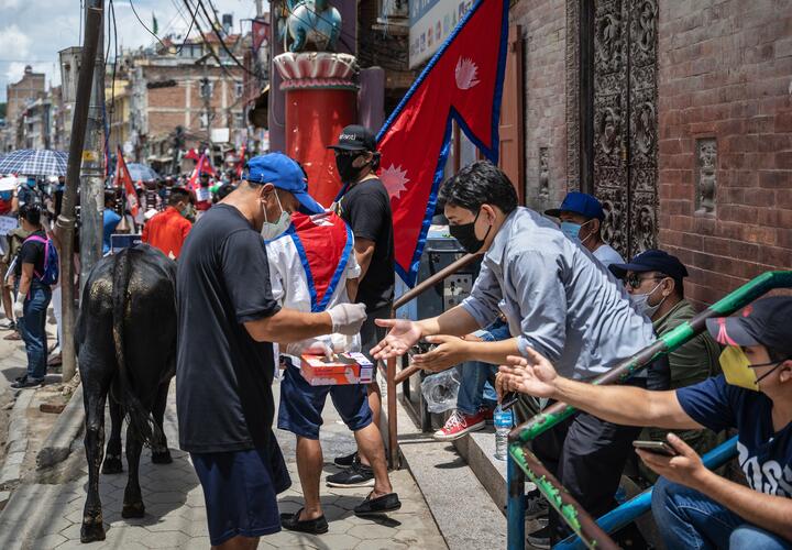 A man in a Covid mask distributes food on a street in Nepal.