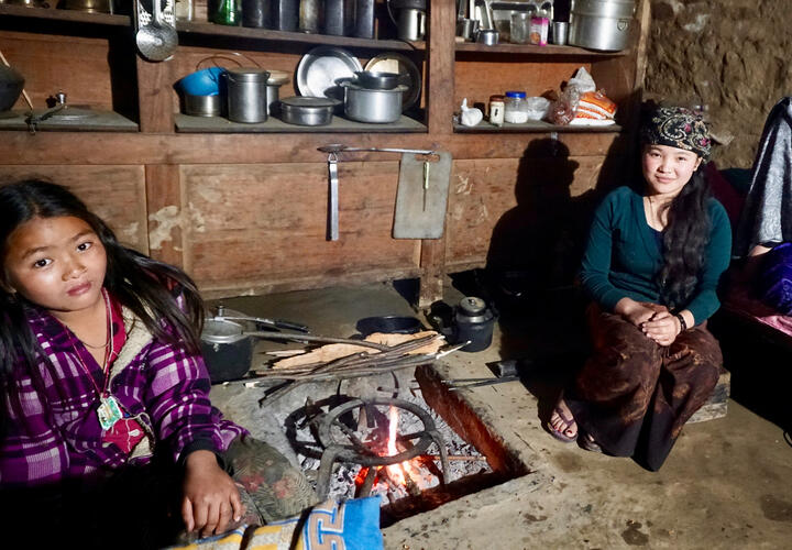Two girls sitting next to cookstove.