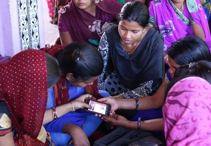 Indian women gathered in a circle using a mobile phone.