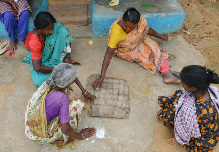 Four Indian women sitting in a circle outside drawing on cardboard.