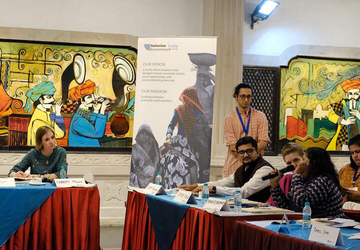 People sitting at various tables, with a woman holding a mic, asking a question.
