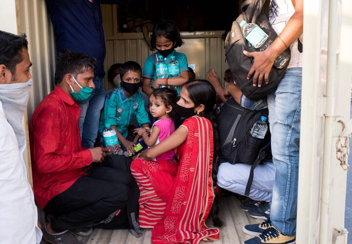 Masked adults and children gathered around doorway with items in their hands. 