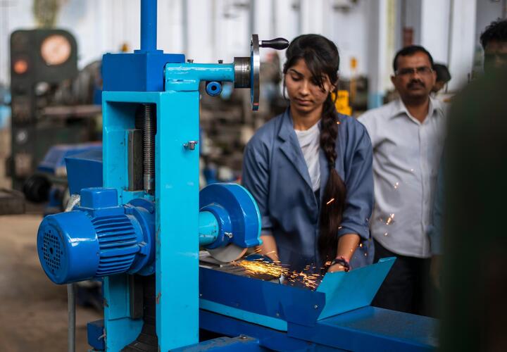 A woman operating a saw in a tech factory in India.