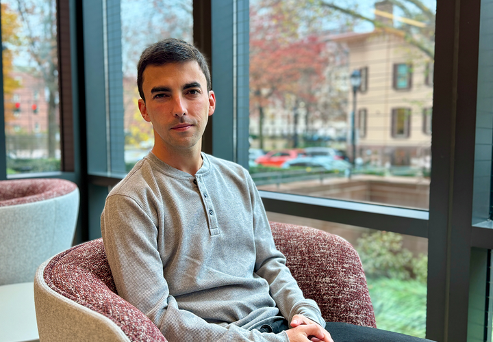 A man in a grey shirt sits in front of a window