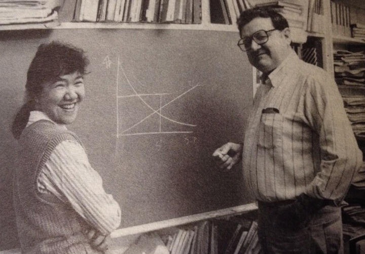 A man and a woman stand in front of a chalkboard (black and white)