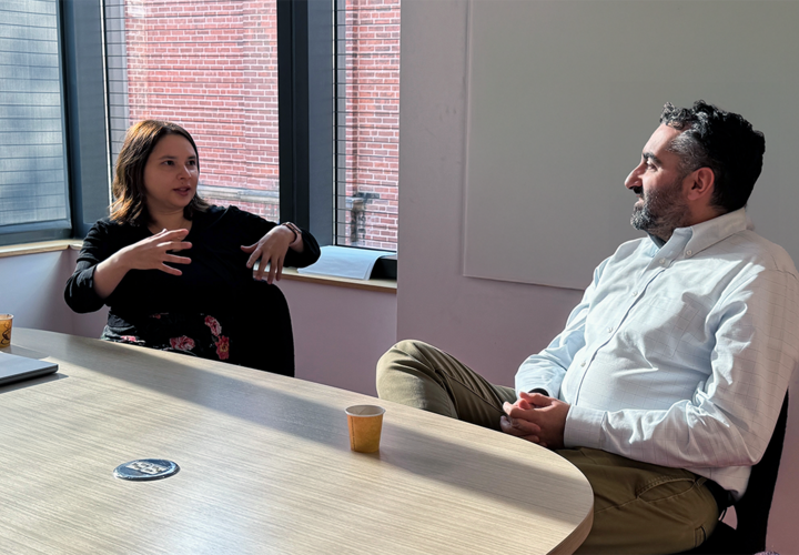 A woman in a black shirt sits down at a table with a man in a white shirt, having an animated conversation