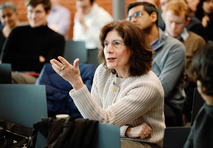 A woman in a tan sweater asks a question during a conference