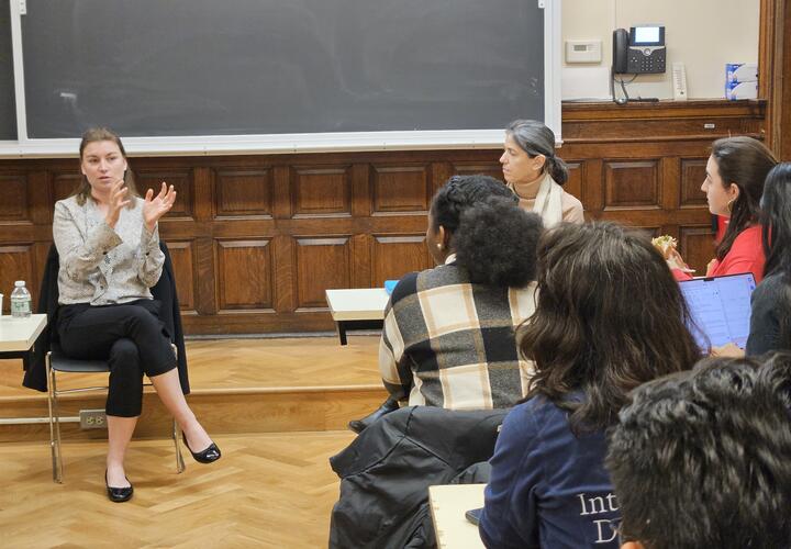 A woman in a grey sweater speaks at the front of a classroom