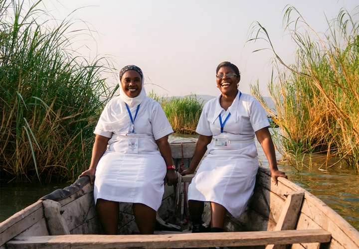 Two women in white nurse uniforms sit smiling in a boat