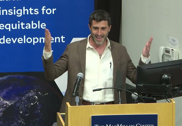 Max Bearak, a man in a white shirt and grey jacket, delivers a lecture at a podium