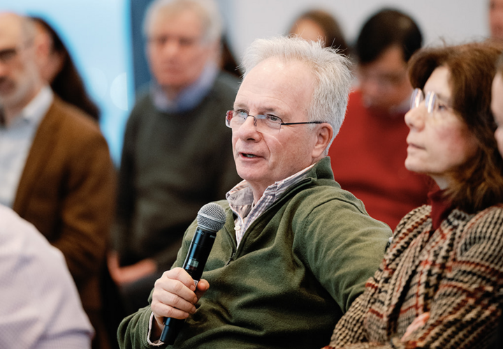 A man in a green sweater asks a question at a presentation