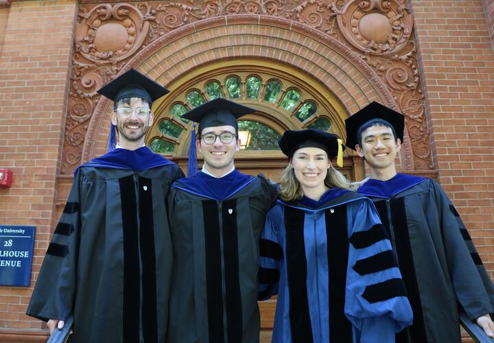 4 graduates on the steps of the Yale Economics Building.