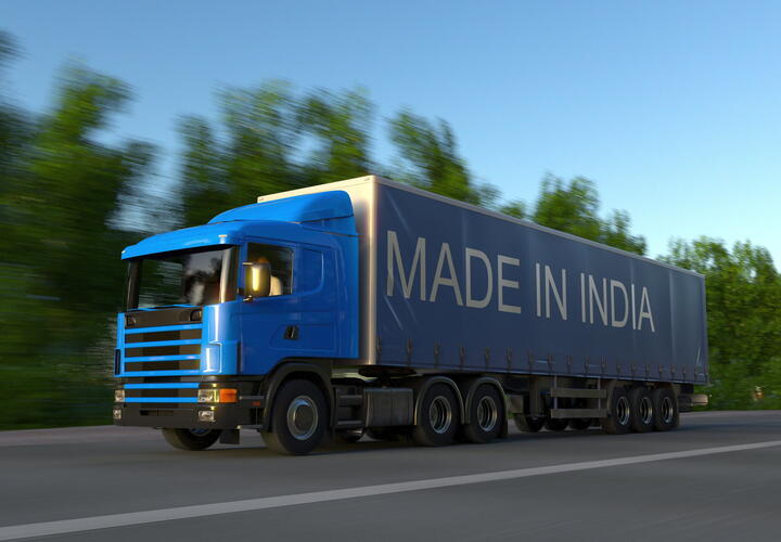 Big blue shipping truck with 'made in India' written on the side driving on the road. 