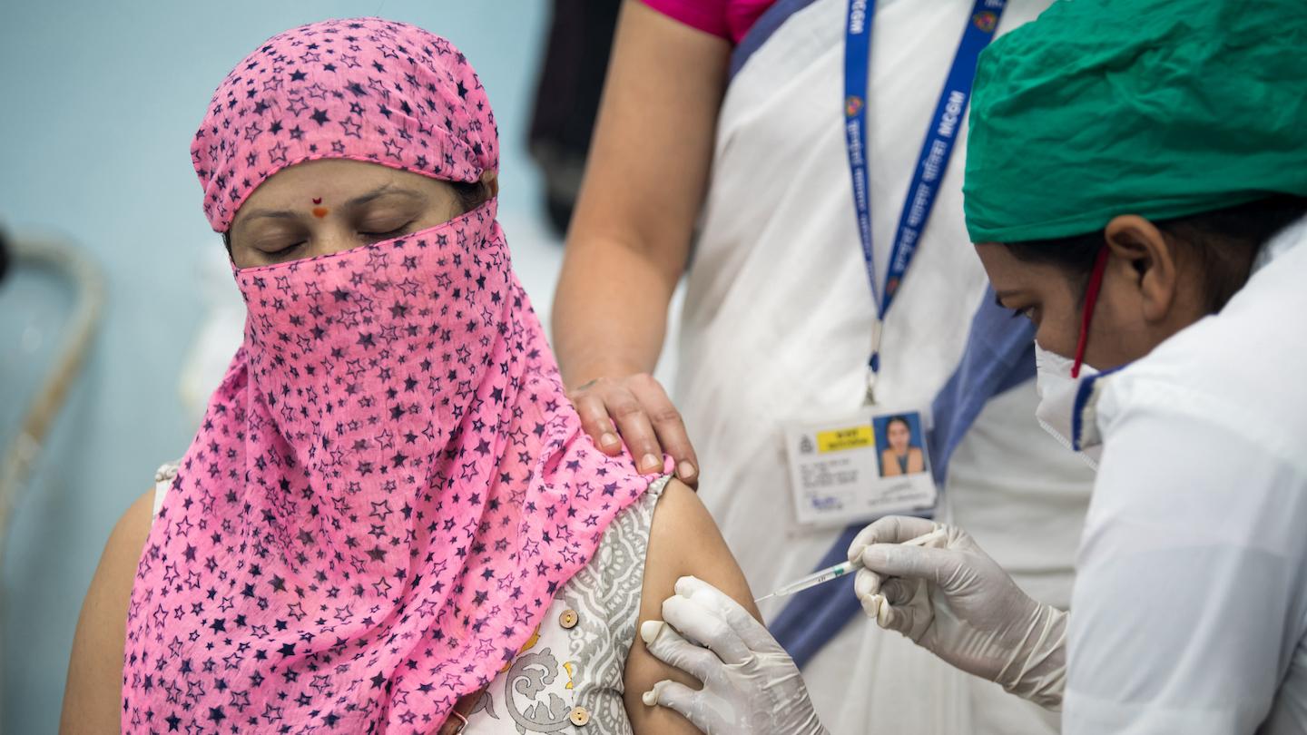 A woman wearing a headscarf receives a vaccine injection from a female health worker.