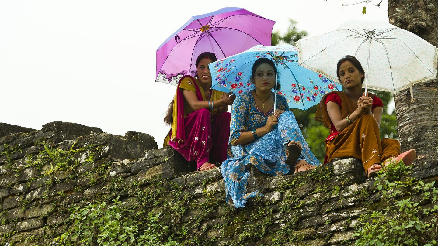 Three women sitting on grass holding umbrellas