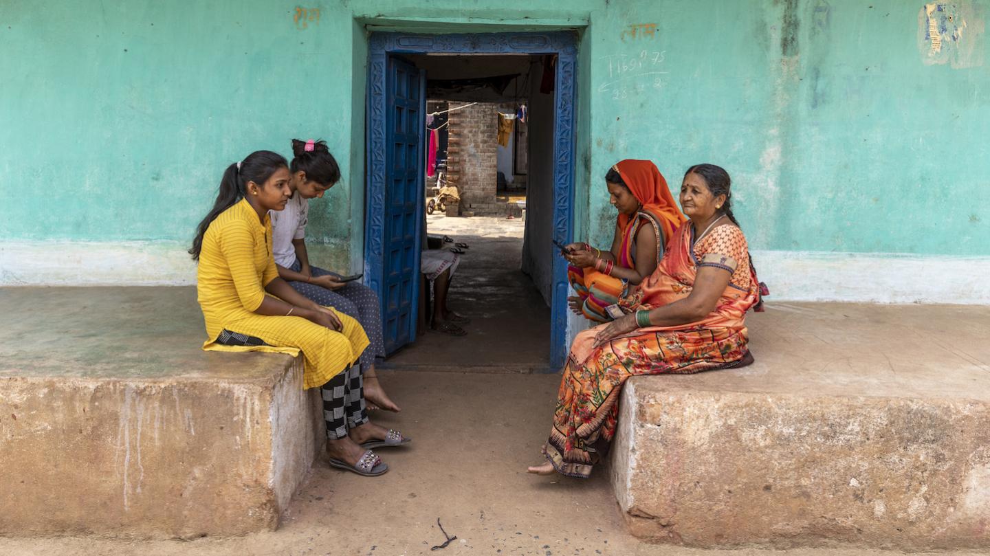 Four women sitting in front of a doorway. Two are using smartphones.