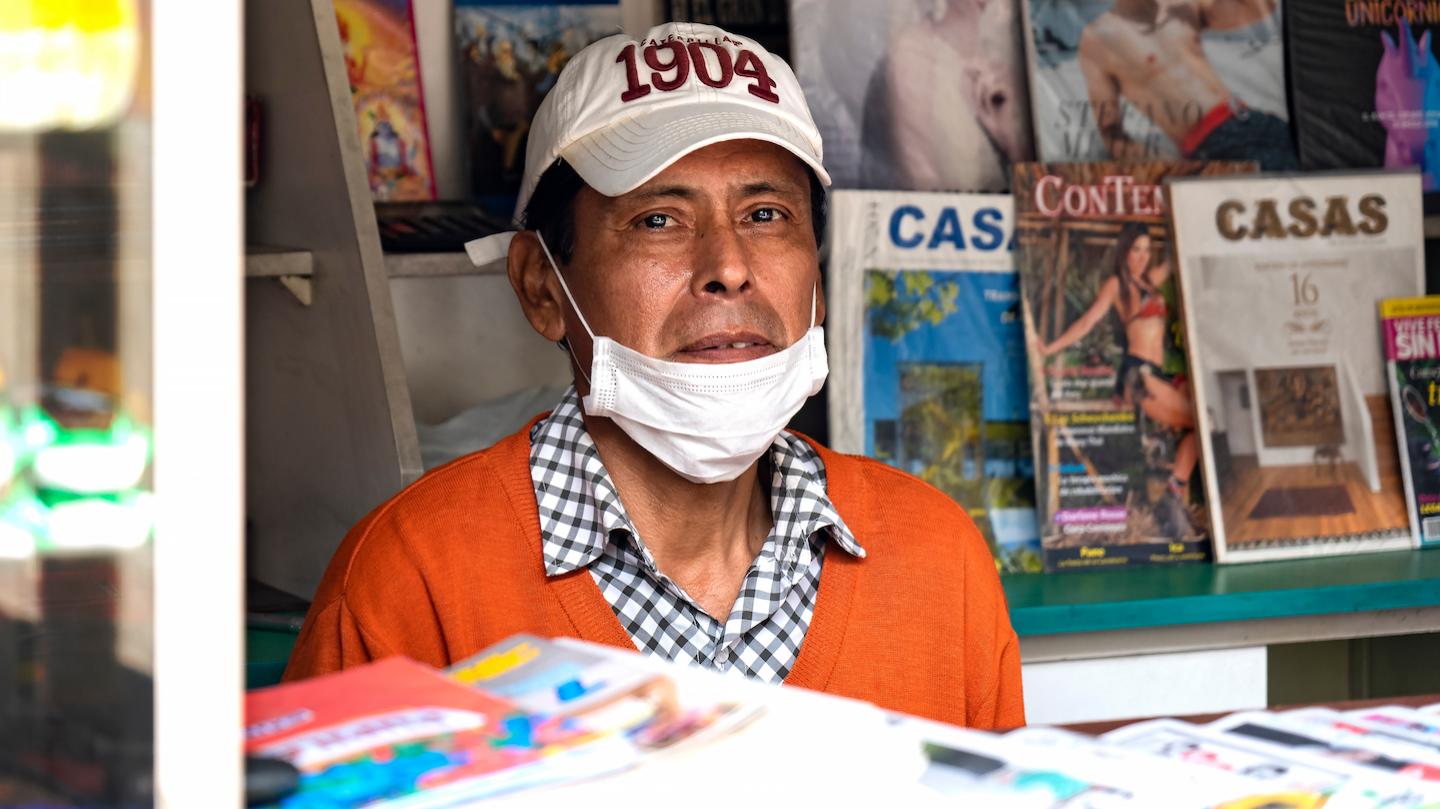 Man in shop booth wearing a mask and a baseball hat