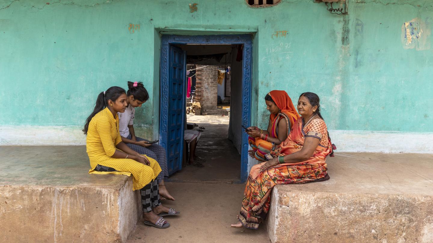 Four women sitting in front of a doorway. Two are using smartphones.