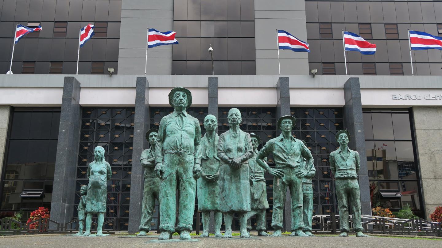 a statue of common people in front of the Central Bank of Costa Rica